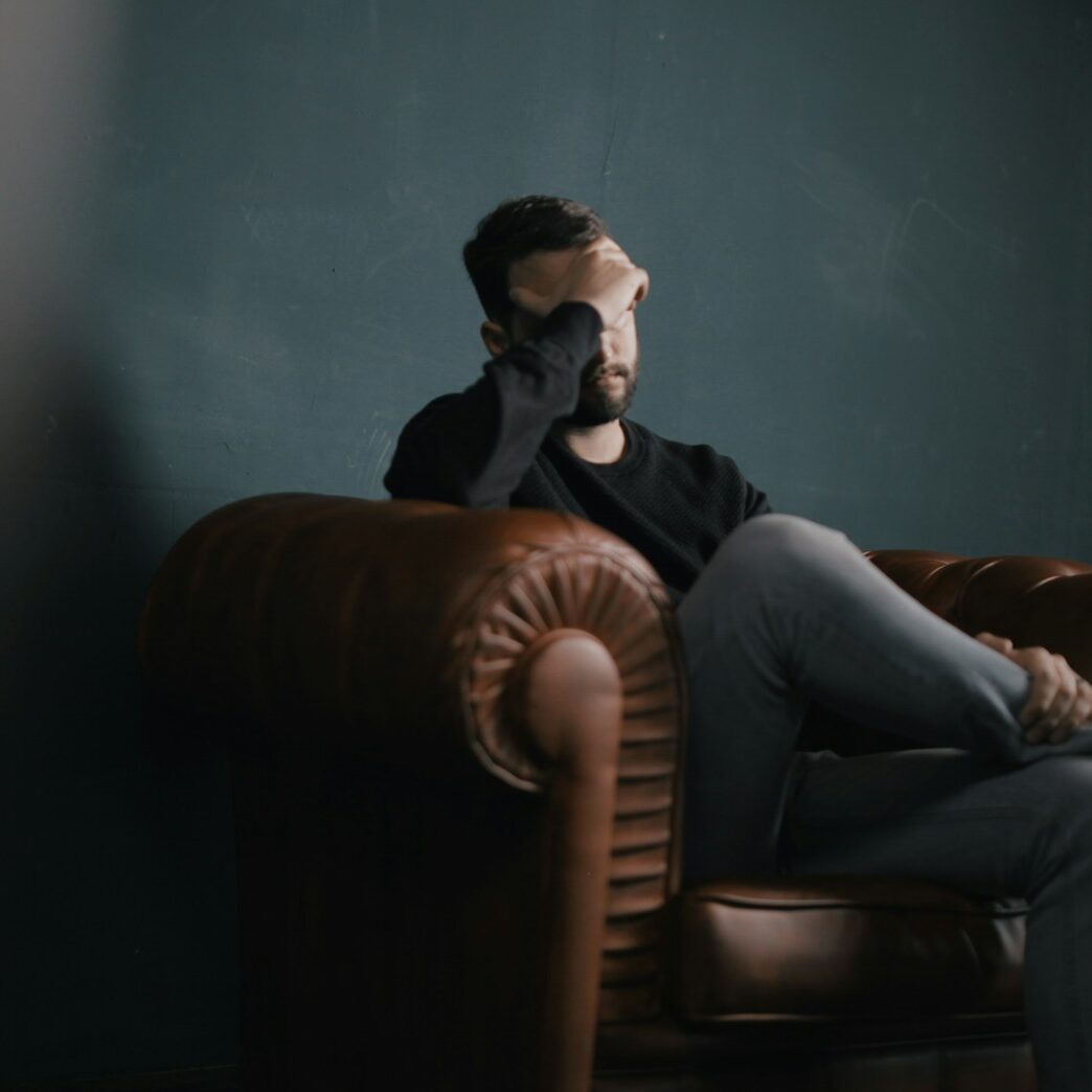 a man holds his head while sitting on a sofa