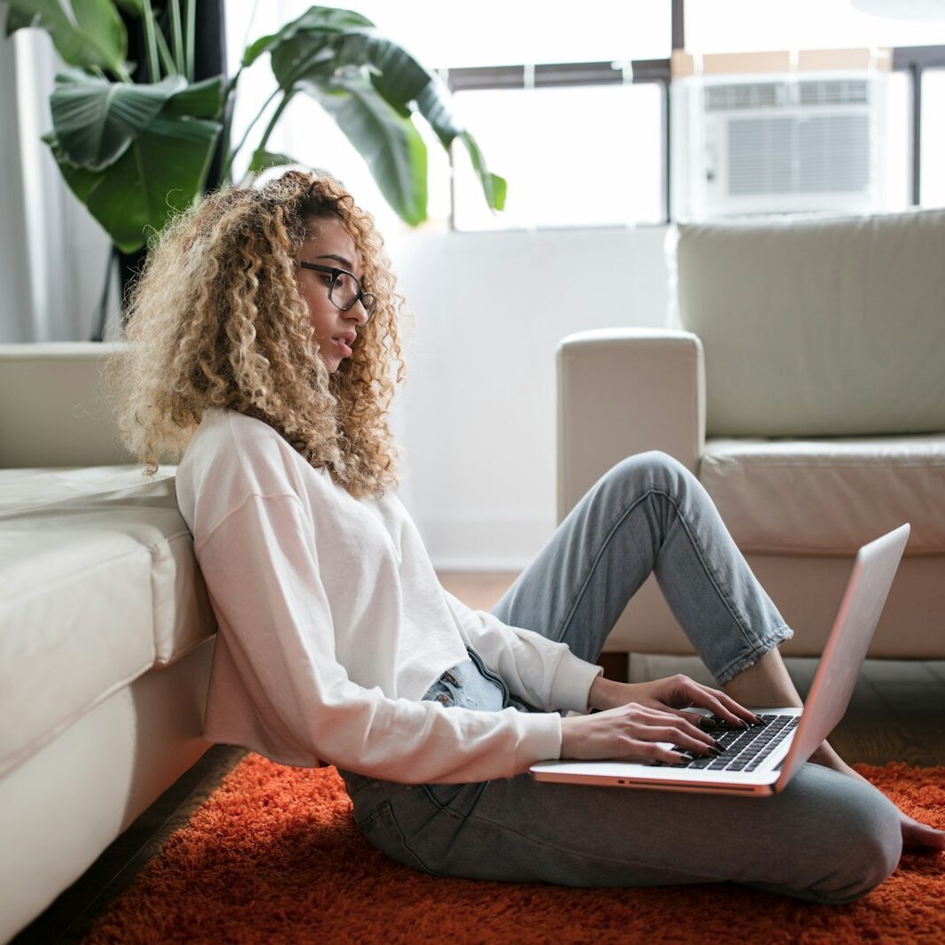 woman sitting on floor and leaning on couch using laptop